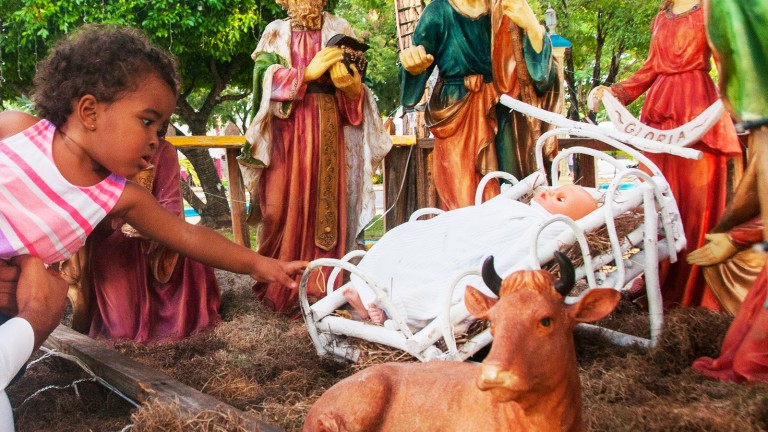 Niña toca nacimiento Niño Jesús en Parque Central de Yaguate, San Cristóbal.