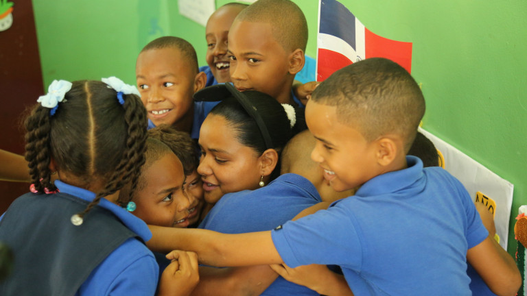 Niños estudiantes se funden sobre su maestra en un abrazo
